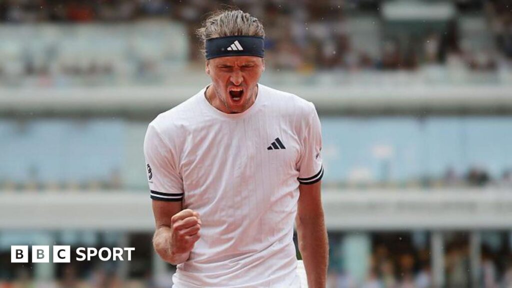 Alexander Zverev, wearing a white t-shirt and black headband, roars with his mouth wide open and clenches his right fist in celebration