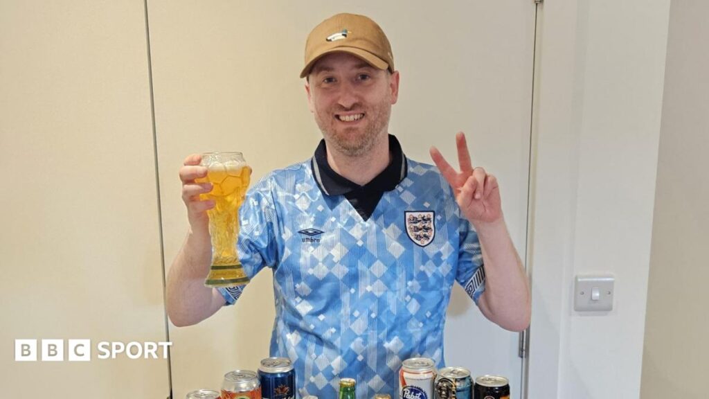 Gus Hully holds a beer in a glass shaped like the World Cup trophy, while he wears a vintage light blue England shirt and a brown baseball cap