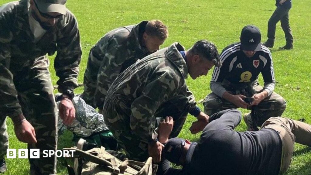 A group including Willy Caballero (left), Aaron Ramsey (second right) and Luke Williams (right) tend to a casualty during a military training exercise as part of the FAW's Uefa pro licence course