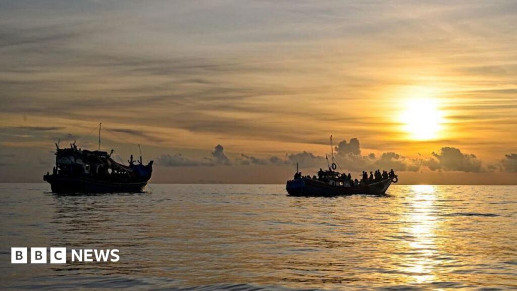 A blue and red boat sailing on the ocean with a sunset in the background with the coast of Indonesia just in view in the left of frame, taken off the coast of Labuhan Haji in Southern Aceh province on October 23, 2024.