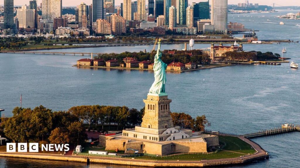 aerial shot of Statue of Liberty and waters surrounding it with New York skyline in background