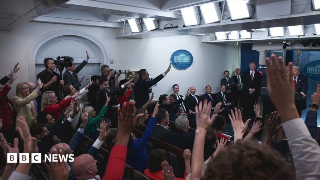 The White House press room full of reporters with their hands raised