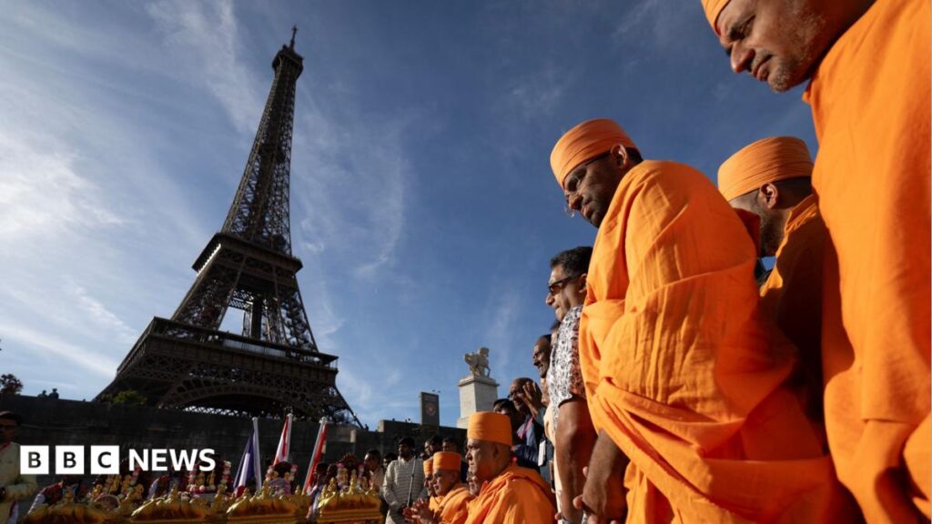 Hindu monks stand in front of the Eiffel Tower wearing traditional orange robes.