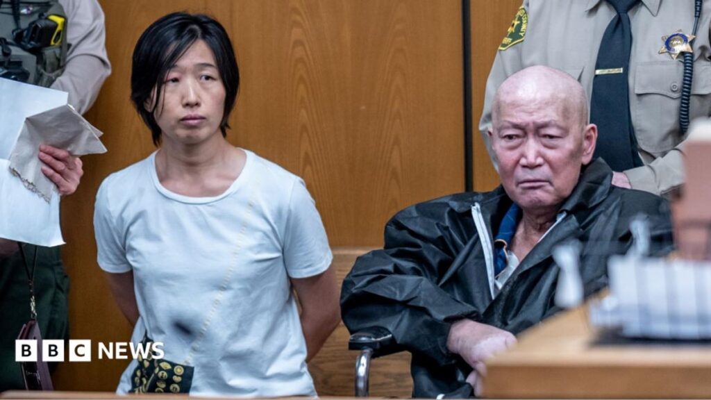 Silvia Zhang, left, and Guojun Xuan, right, sitting in Pasadena courtroom with two sheriffs standing behind them. Zhang has her hand behind her back and is wearing a blue shirt while Xuan is wearing a black jacket
