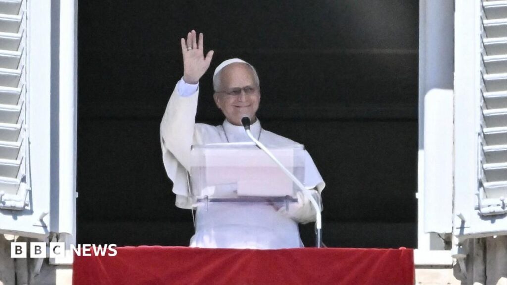 Close-up of Pope Leo's face with raised hand, as he leaves after a Mass on Sunday 2 May